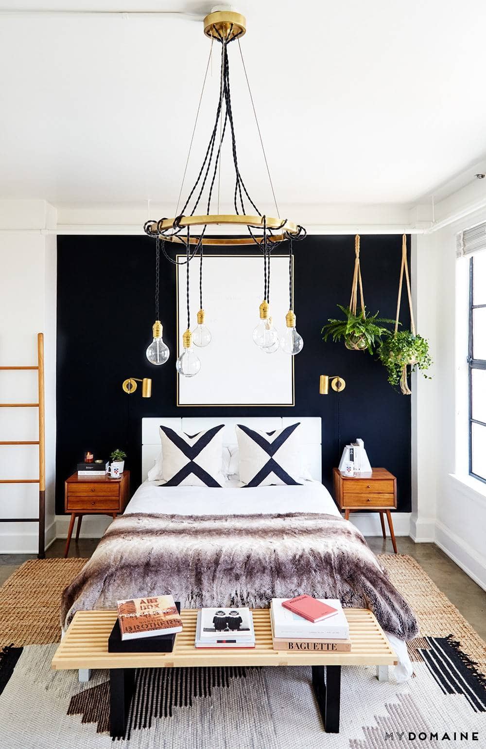 Black focus wall behind bed, hanging bulb chandelier and white bed.